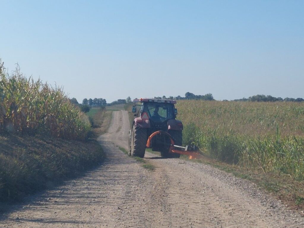 droga żwirowa wśród pól - traktor kosi pobocze